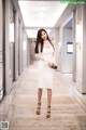 A woman in a white dress standing in a hallway.