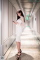 A woman in a white dress standing in a hallway looking at her phone.