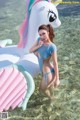 A woman in a blue swimsuit standing next to an inflatable unicorn.