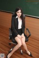 A woman sitting on a chair in front of a blackboard.