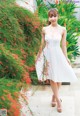 A woman in a white dress standing in front of red flowers.