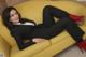 A woman in a black suit and red boots laying on a yellow couch.