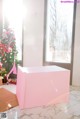 A pink box sitting in front of a window next to a Christmas tree.