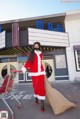 A woman dressed as Santa Claus pushing a shopping cart.