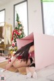 A woman in a santa claus outfit is sitting in a pink box.