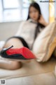 A woman sitting on a couch with a pair of red shoes.