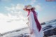 A woman with pink hair wearing a straw hat on the beach.