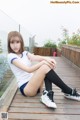 A young woman sitting on a wooden deck with her legs crossed.