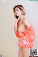 A woman in an orange kimono talking on a cell phone.