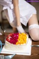 A woman in a white dress is putting fruit on a cake.