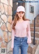 a woman wearing a pink shirt and jeans standing in front of a stone wall