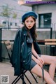 A woman sitting on a chair wearing a black jacket and a blue beret.