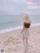 A woman walking on the beach with a straw hat on her head.