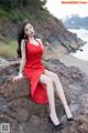 A woman in a red dress sitting on a rock by the ocean.