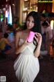 A woman in a white dress holding a pink cell phone.