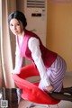 A woman in a red vest and striped skirt sitting on a red chair.