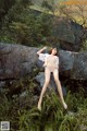 A woman in a bikini posing on a rock in the woods.