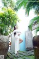 A woman in a white dress posing in front of a blue wall.